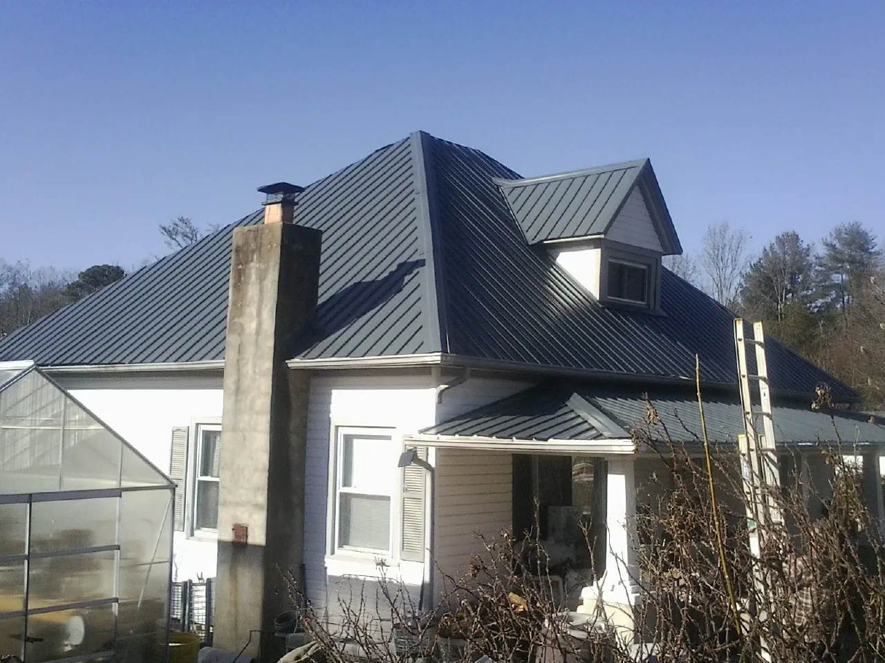 Dark blue standing seam metal roof on a white farmhouse with dormer — Slate & Tile Roof Repair by Roofing Brothers in Bulls Gap