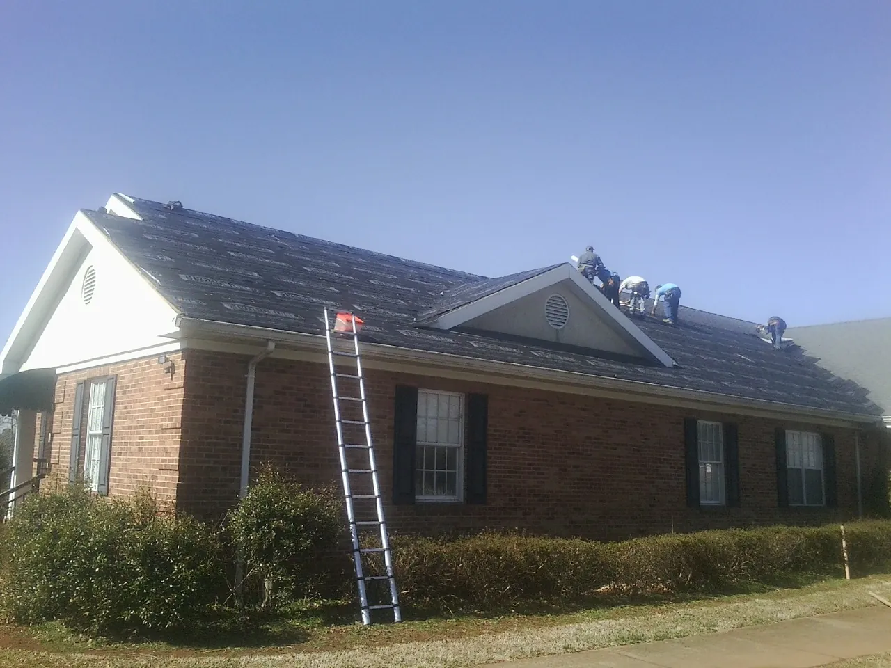 Crew tearing shingles off a brick ranch roof with a ladder set — Emergency Roof Repair work by our crew in Bulls Gap