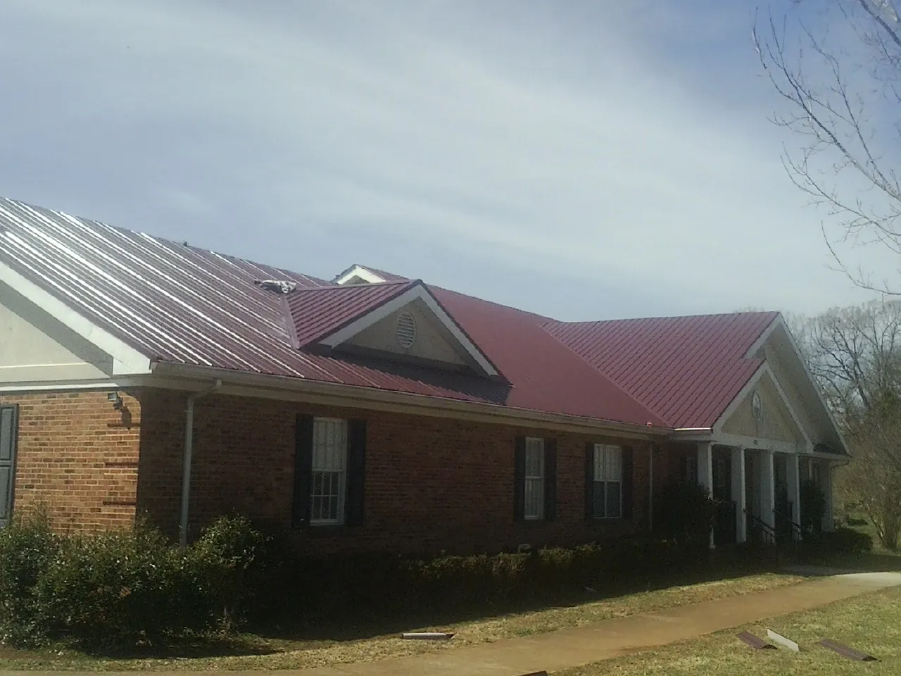 Red metal roof with gabled entries on a long brick building, from a Hail Damage Roof Repair job in Bulls Gap
