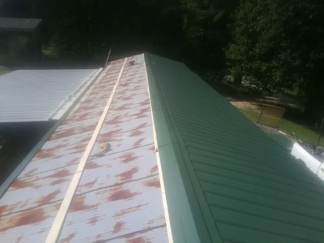 Old rusted panels beside newly installed green metal roofing — Wind Damage Roof Repair by Roofing Brothers in Bulls Gap