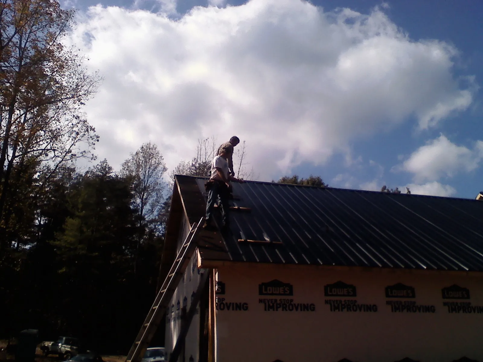 Roofer fastening dark metal panels high against a cloudy sky, from a Roof Inspection job in Bulls Gap