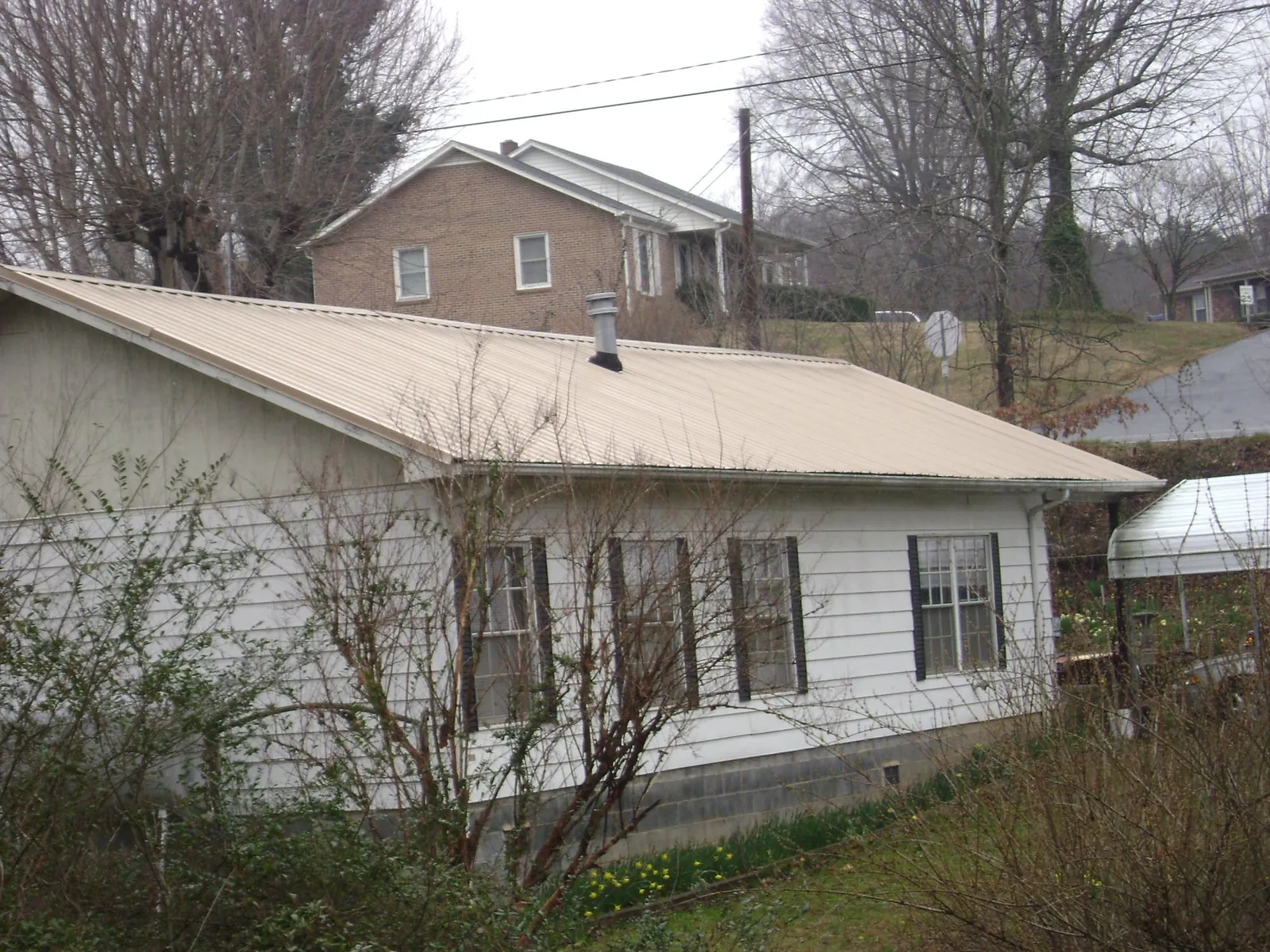 Tan metal roof on a white sided house set into a hillside — Commercial Roofing by Roofing Brothers in Bulls Gap
