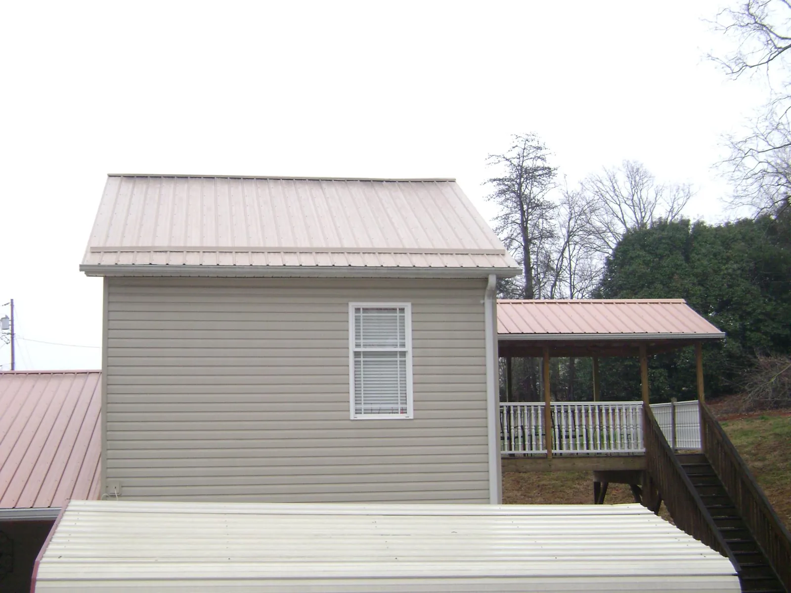Tan metal roofs on a two story addition and attached porch, from a Roof Replacement job in Bulls Gap